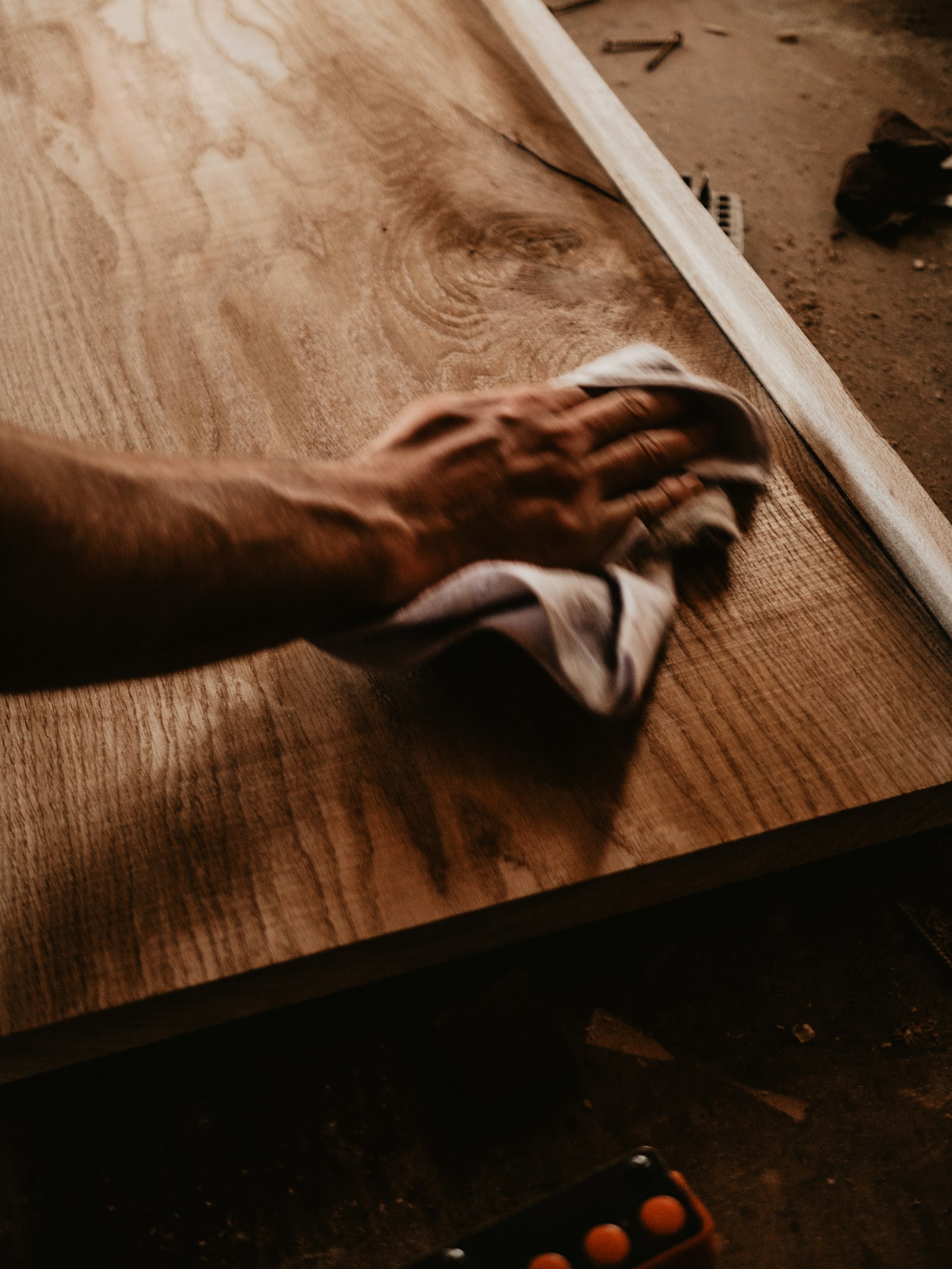 A hand wiping a wooden surface with a white cloth.