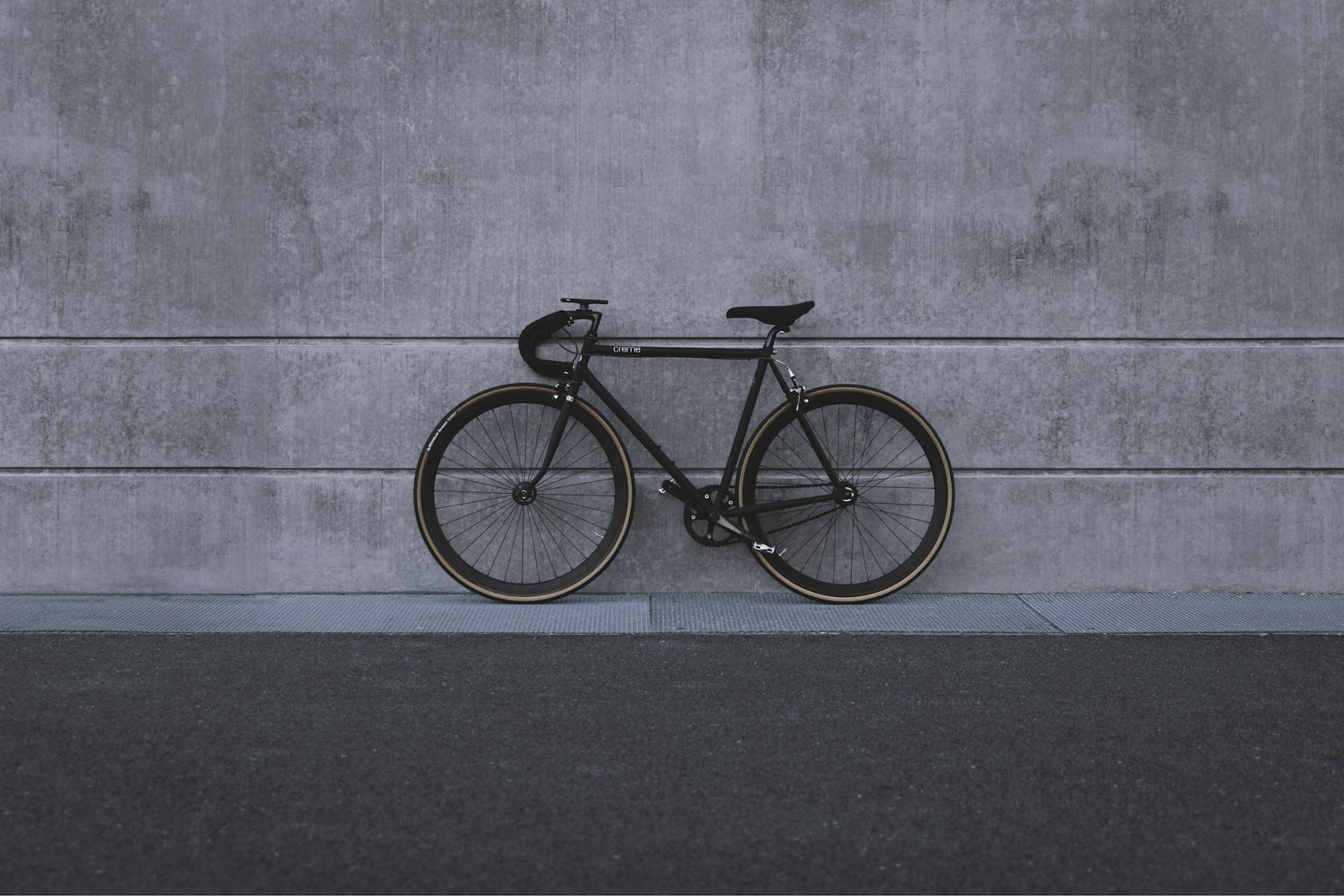 Black single-speed bicycle leaning on a grey concrete wall