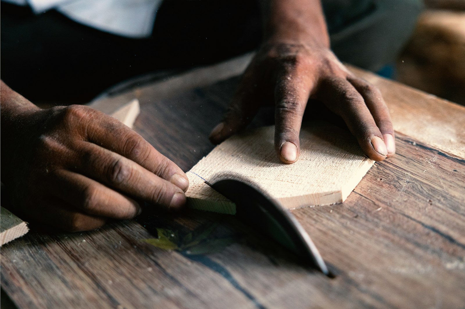 Hands carving a block with a blade on a wooden bench