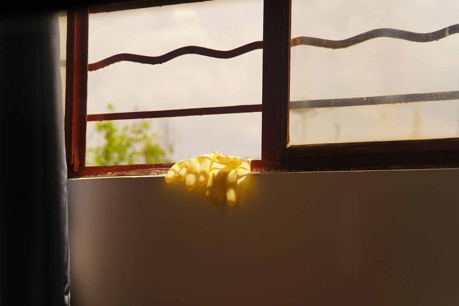 Yellow rubber gloves resting on a sunny windowsill.