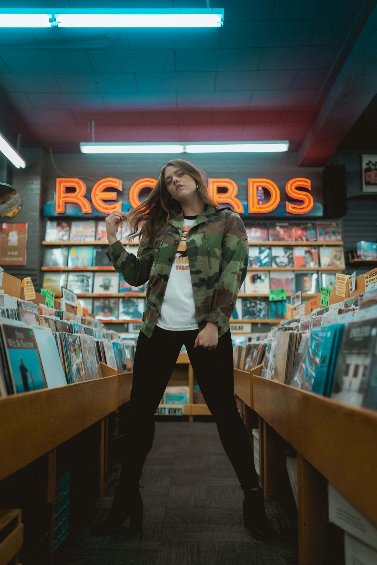 Woman standing in a record shop aisle under a neon RECORDS sign