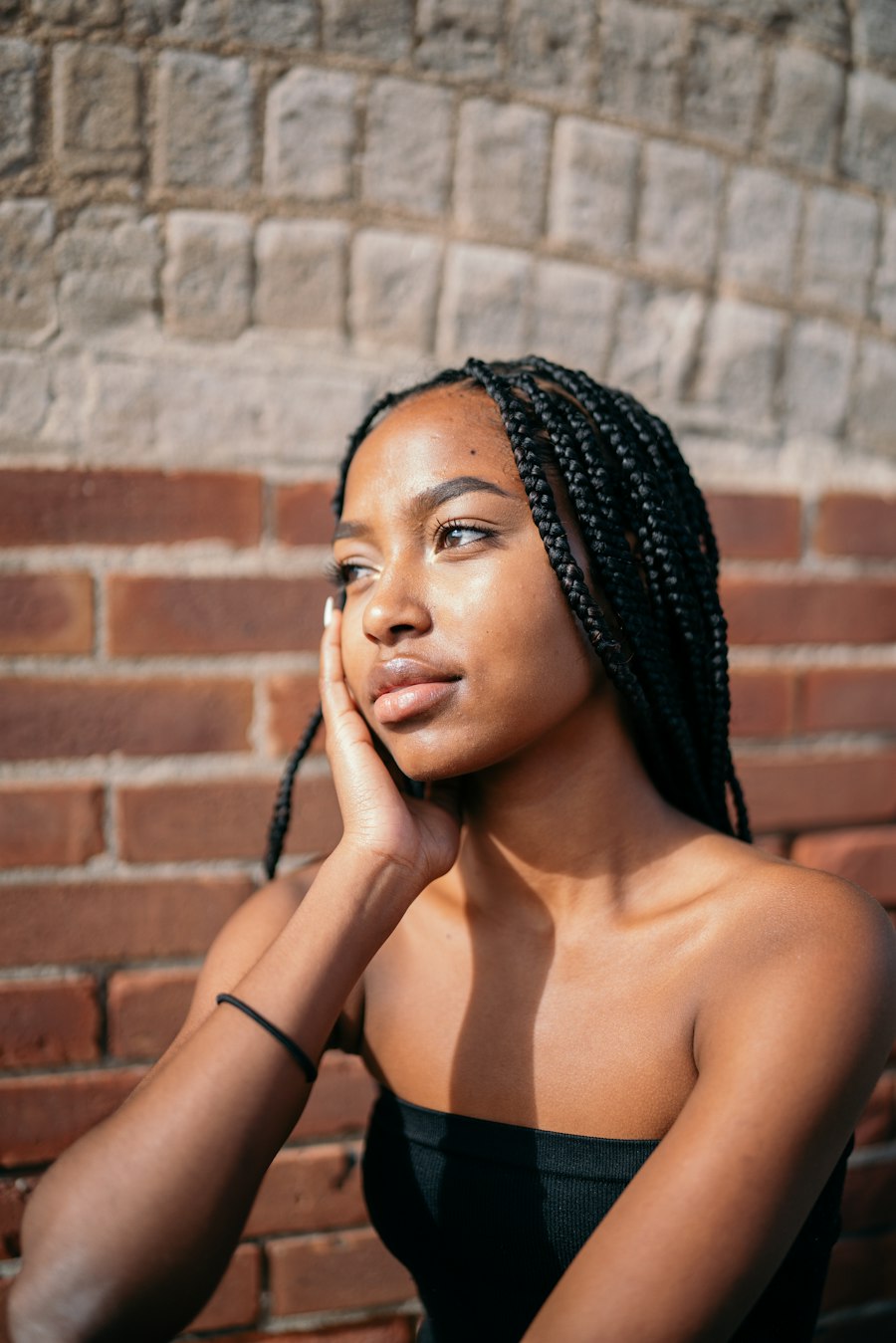 Portrait of a woman with long braids against a brick wall