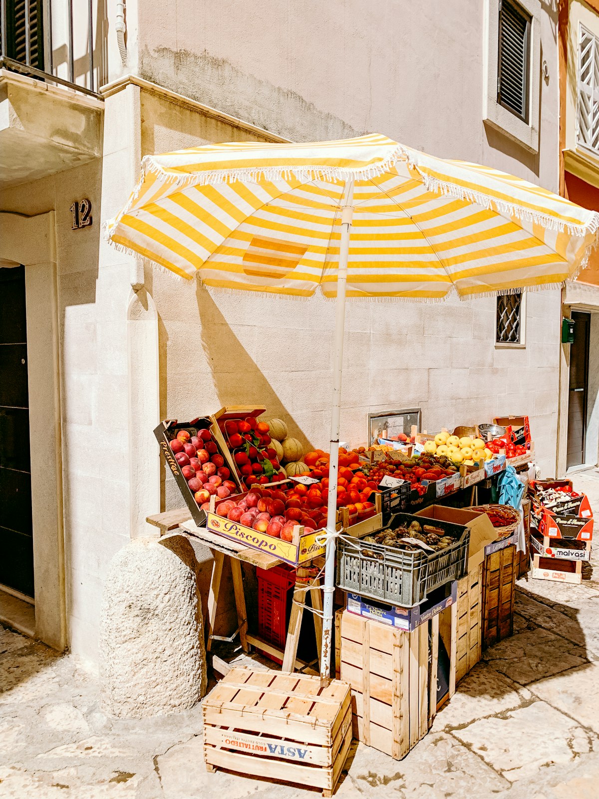 Farm stand with fruit crates under a striped umbrella