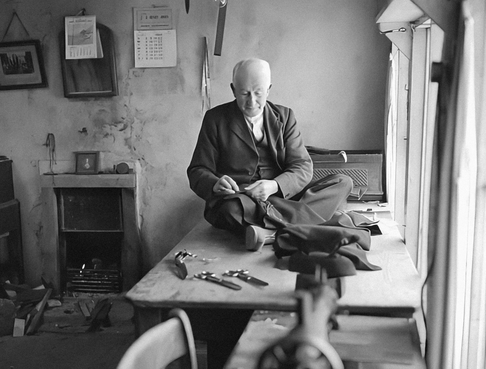 Tailor sitting on the bench hand-sewing a garment
