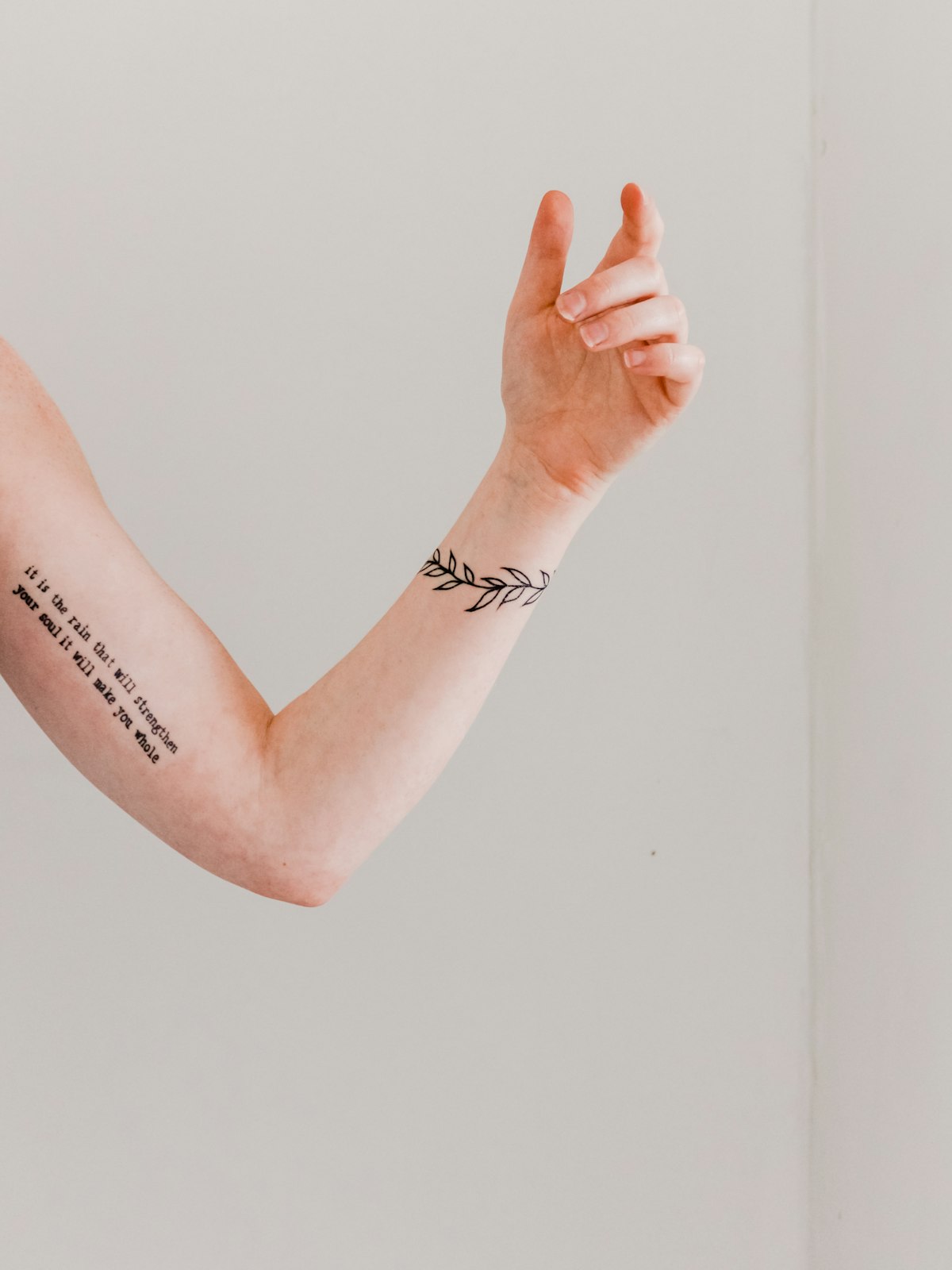Fine-line script and a leaf band tattooed along an arm