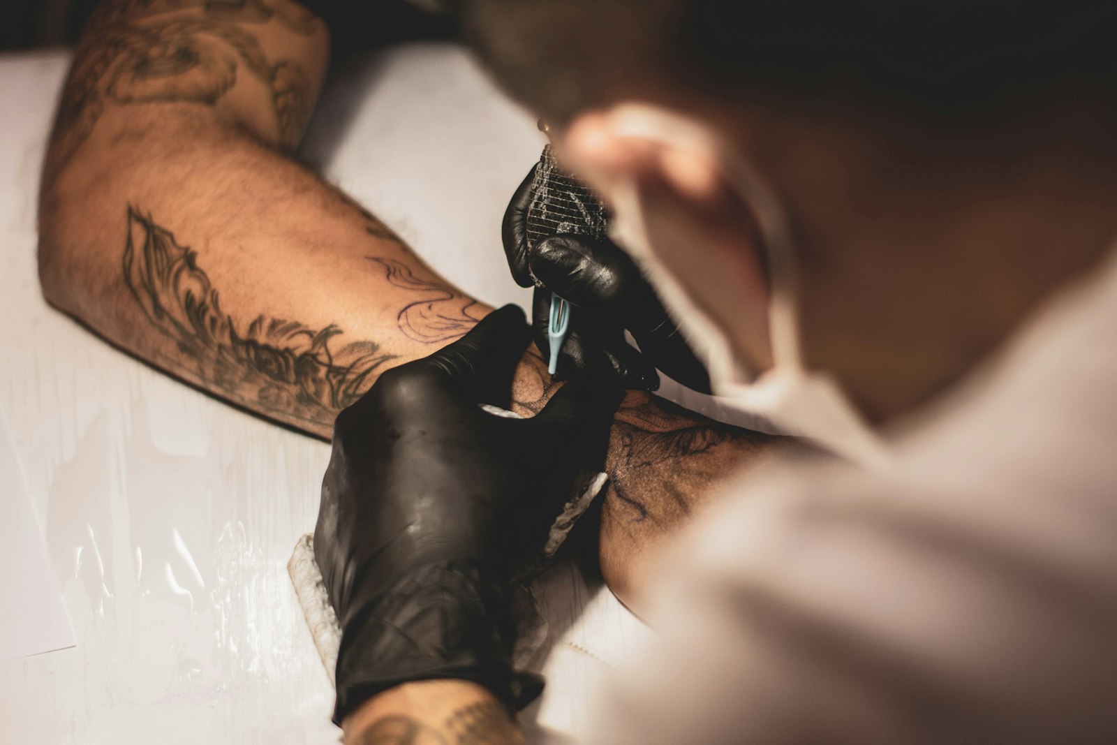 Tattoo artist in black gloves tattooing a client's forearm