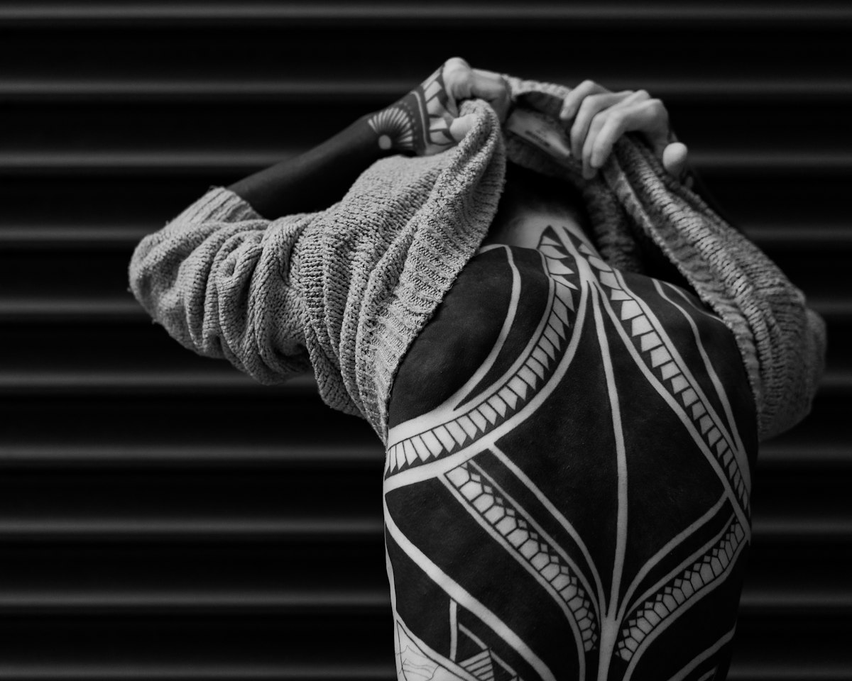 Bold blackwork tattoo across a person's back, sweater pulled over the head